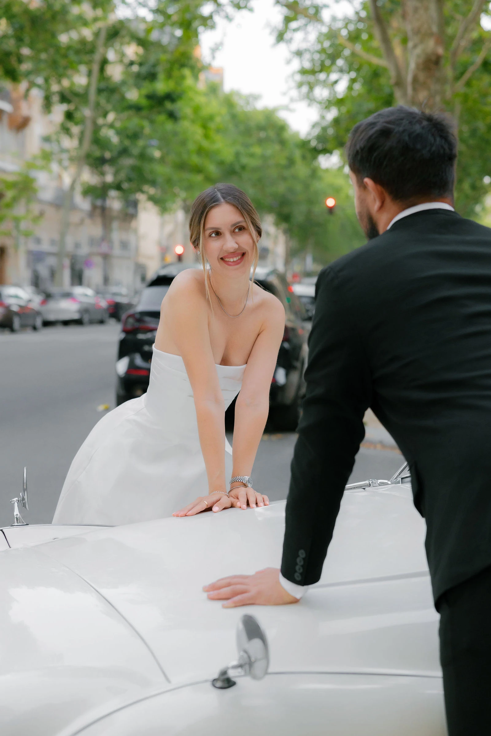 Julia leaning on a vintage car bonnet while Anatoly looks on, Paris