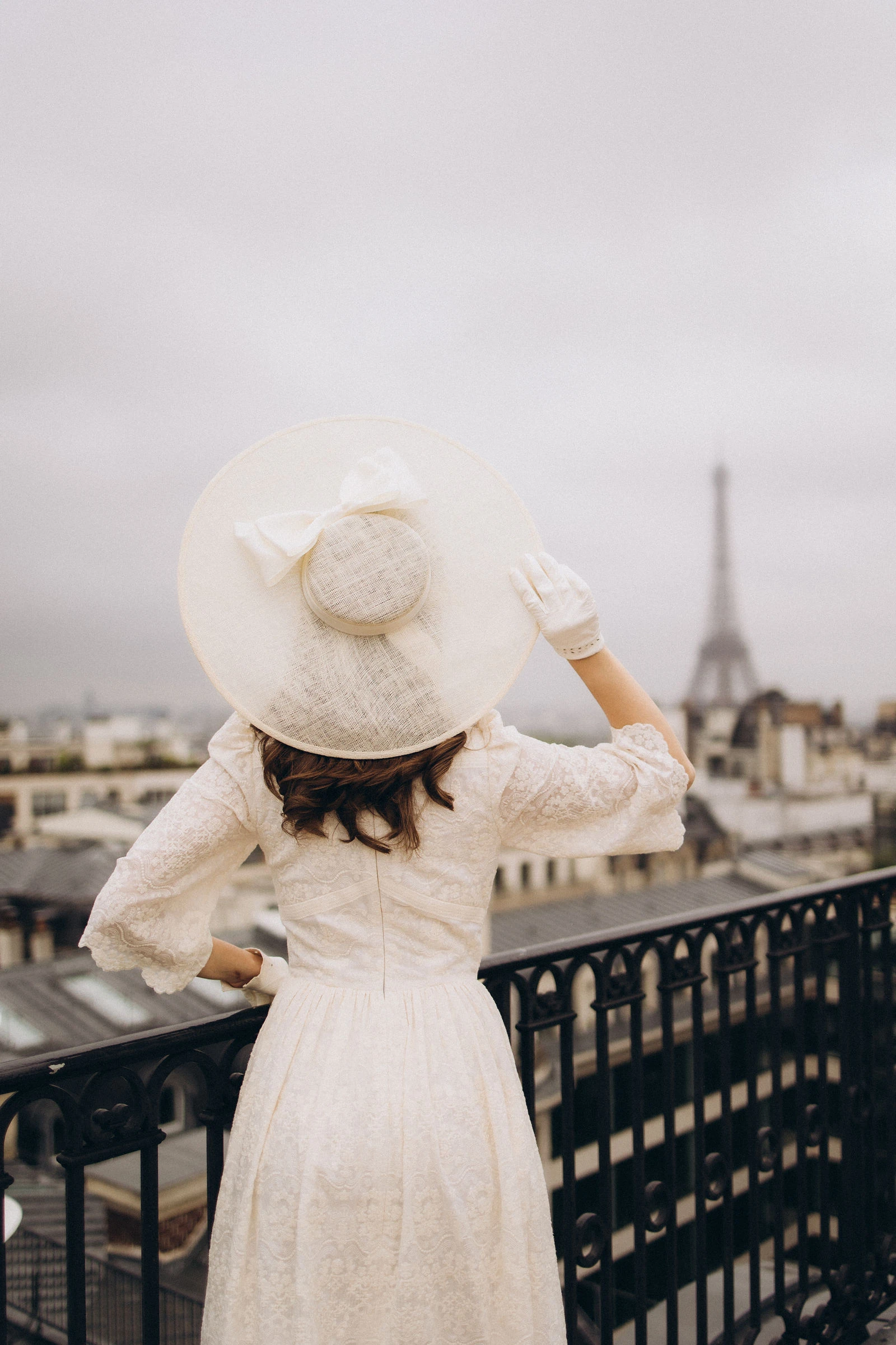 Bride in a wide hat on a Paris rooftop facing the Eiffel Tower