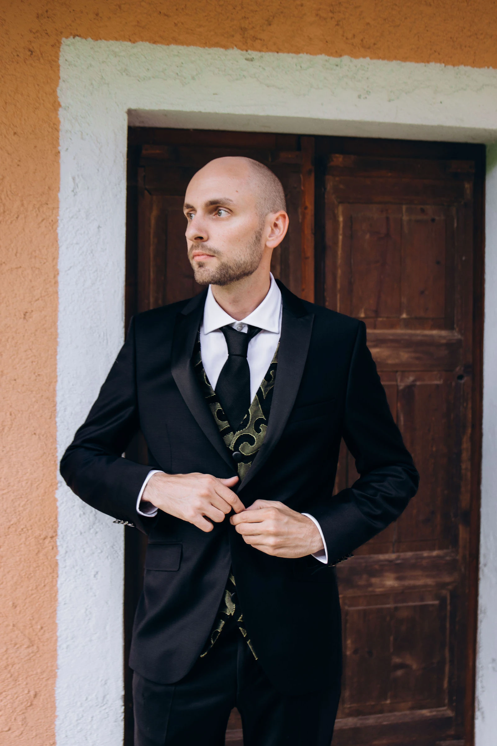 Groom buttoning his jacket in a courtyard doorway