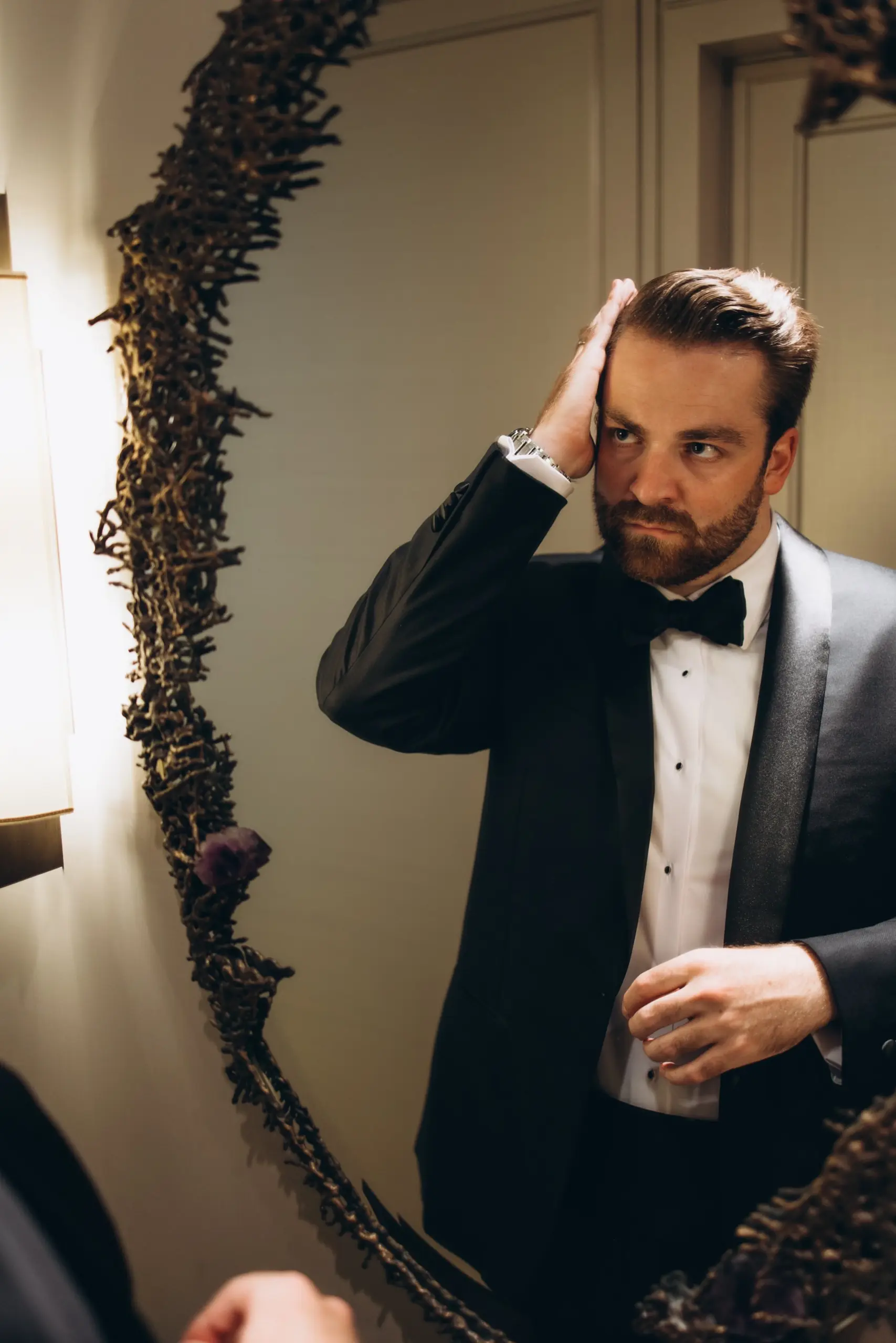 Groom fixing his bow tie in the mirror